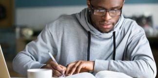 Closeup smart millennial african student wear glasses hold pen noting writing down information study use book preparing for university or college test exam, horizontal photo banner for website header