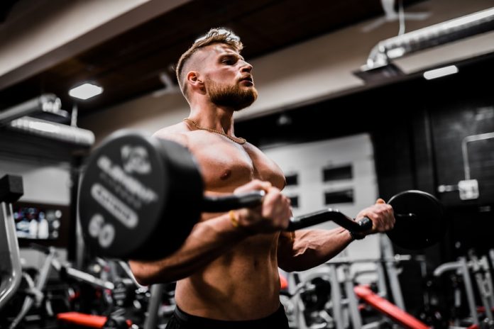 Photo by Anastase Maragos topless man in black shorts carrying black dumbbell