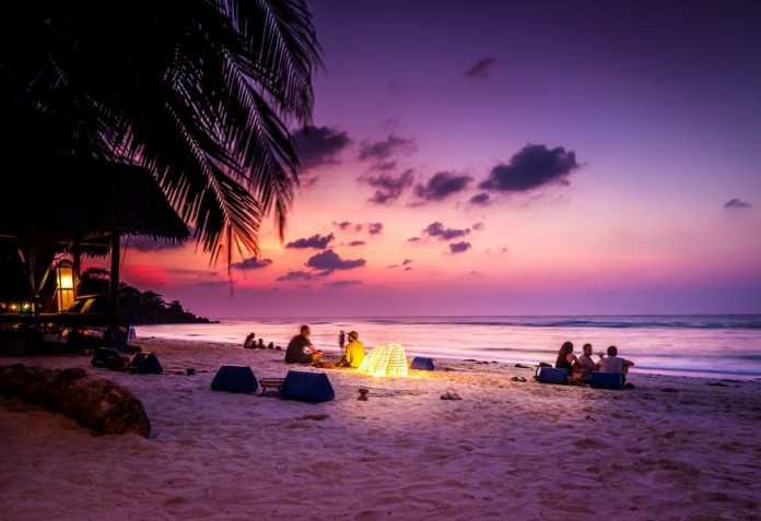 Photo by cmophoto.net people sitting near seashore viewing sea under orange and blue skies