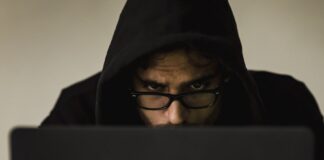 Serious young male programmer wearing black hoodie browsing netbook and hacking software in studio