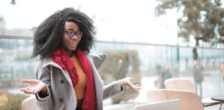Happy excited African American female laughing and gesticulating while having video calling on laptop and sitting at modern cafe