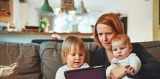 two babies and woman sitting on sofa while holding baby and watching on tablet