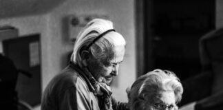 greyscale photo of woman standing behind woman sitting on chair