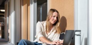 woman in white long sleeve shirt and blue denim jeans sitting on brown wooden table using