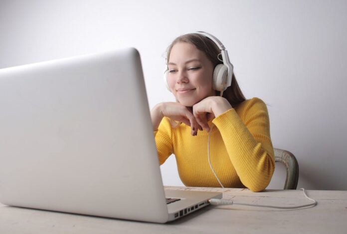 Free Woman in Yellow Sweater Wearing Headphones Using Laptop Stock Photo