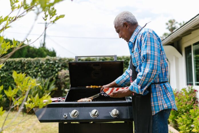 Photo by RDNE Stock project An elderly man grilling sausages on a barbecue in his backyard on a sunny day.