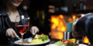 Couple enjoying a cozy dinner with steak and red wine in a warm, intimate setting.
