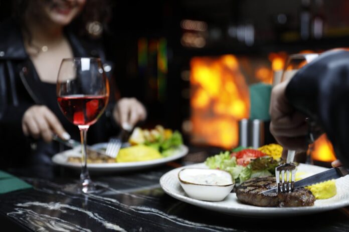 Photo by Nasim Didar Couple enjoying a cozy dinner with steak and red wine in a warm, intimate setting.