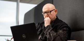 a bald man sitting in front of a laptop computer