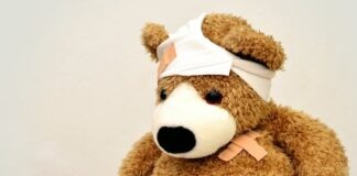 A brown teddy bear with bandages, depicting a playful take on injury recovery in a minimalist setting.