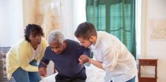 An elderly man receiving assistance from caregivers in a cozy home environment.