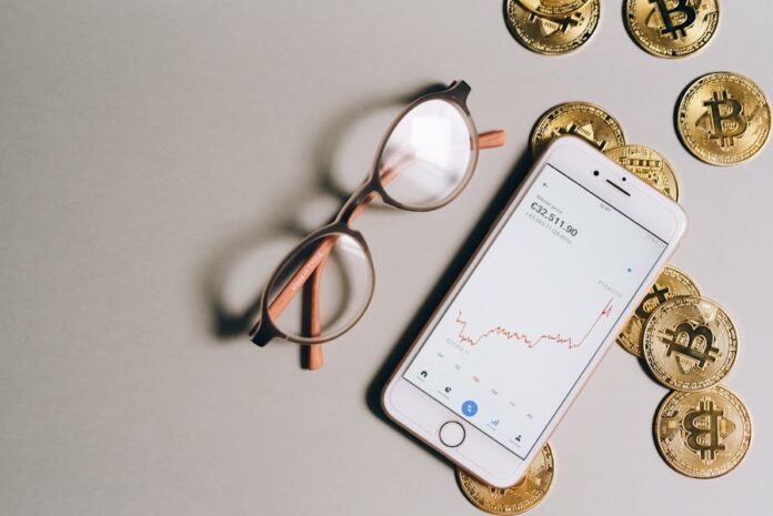 Flat lay of Bitcoin coins, eyeglasses, and smartphone displaying cryptocurrency graph.