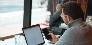 man sitting near table with laptop and smartphone near window