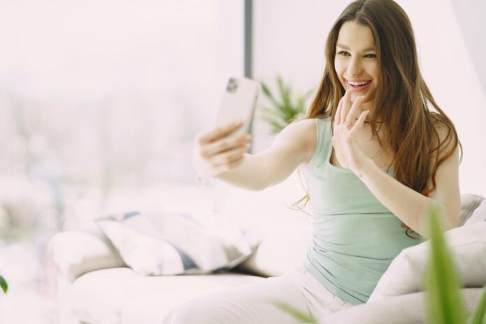 Woman sitting on sofa making a video call, enjoying a bright day at home.