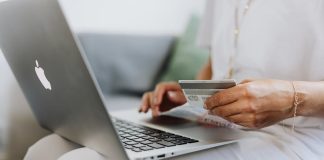 Close-up of a person holding a credit card while shopping online using a laptop at home.