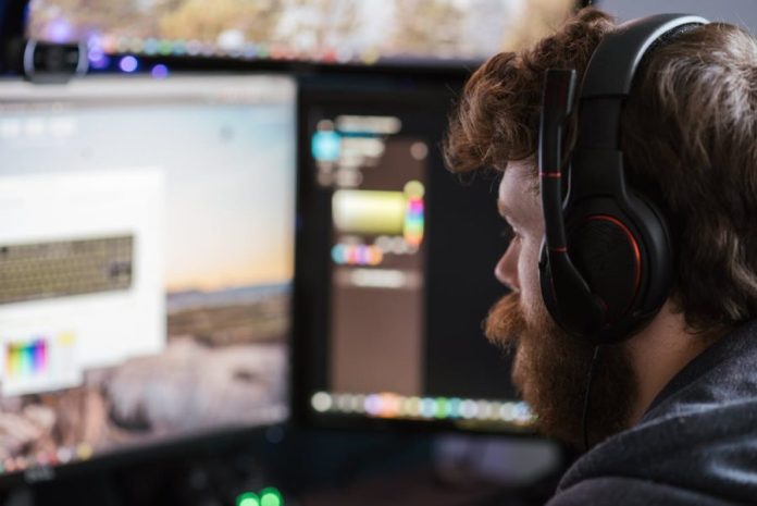 free-man-with-headset-concentrating-on-work-at-dua Free Man with headset concentrating on work at dual monitors in a home office setting. Stock Photo