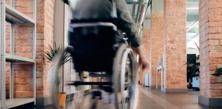 Blurred motion of a person in a wheelchair moving quickly through an indoor office hallway.