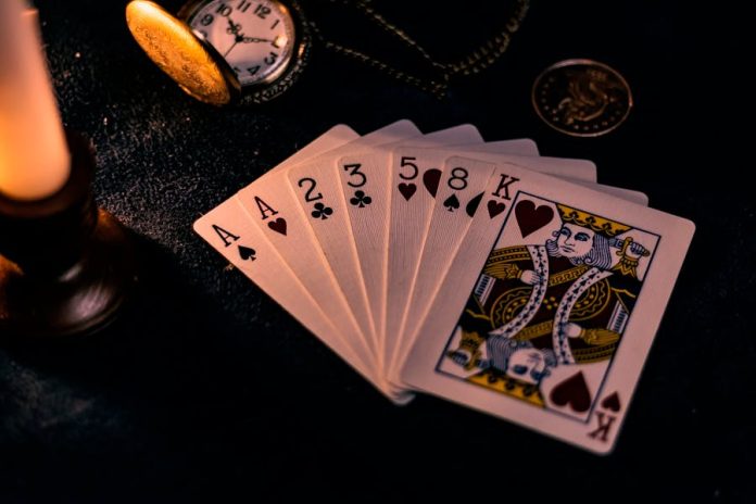 Photo by Kendall Hoopes A dimly lit close-up of playing cards with a pocket watch, showcasing a nostalgic casino vibe.