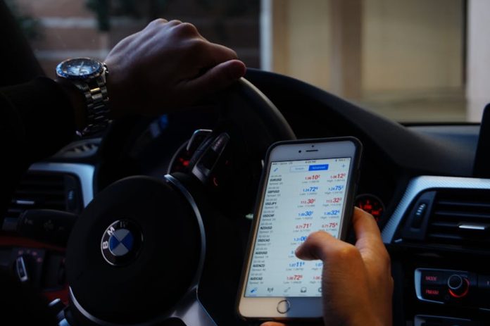 Photo by D'Vaughn Bell Person using mobile phone for currency trading while driving BMW car.