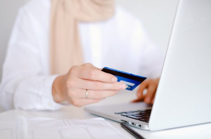 Photo by Anna Shvets Close-up of a person holding a credit card while using a laptop for online shopping.