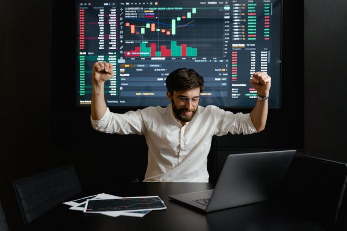 Photo by Tima Miroshnichenko Businessman celebrates stock market success with hands raised in excitement at a trading desk.