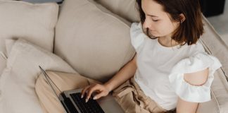 Young woman engaged in remote work on a laptop, sitting on a beige couch indoors.