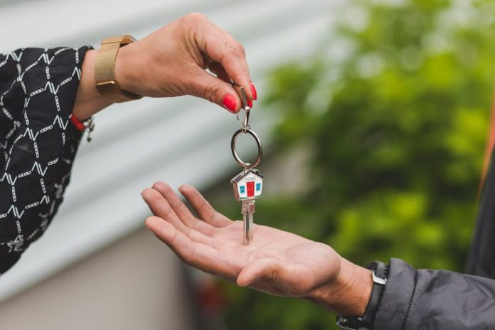 Photo by RDNE Stock project Close-up of a hand handing over a key with a house keychain, symbolizing real estate transaction.