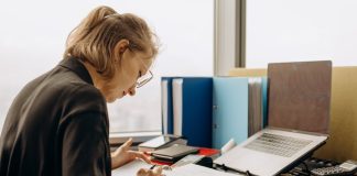 Woman in glasses intensely working at a desk with documents and a laptop.
