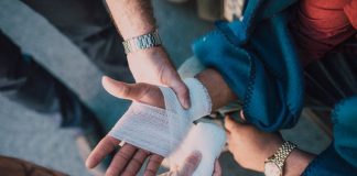 Close-up of two people bandaging an injured hand outdoors, focusing on first aid care.