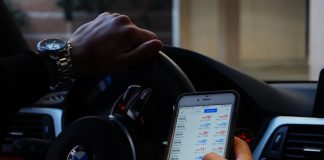 Person using mobile phone for currency trading while driving BMW car.