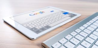 A modern tablet displaying a search engine logo next to a wireless keyboard on a wooden desk.
