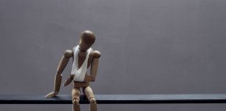 A wooden mannequin sits sadly with a bandage.