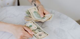 Close-up of hands counting US dollar bills on a marble table surface.
