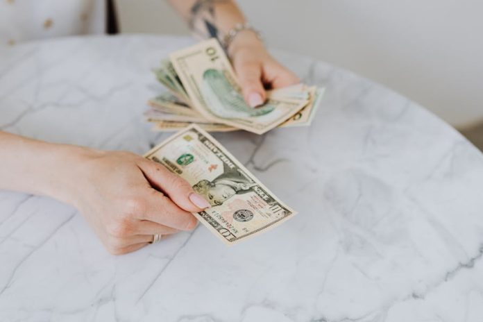 Photo by Photo By: Kaboompics.com Close-up of hands counting US dollar bills on a marble table surface.