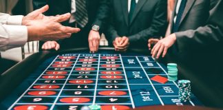 Group of people playing roulette, placing bets in a casino setting.