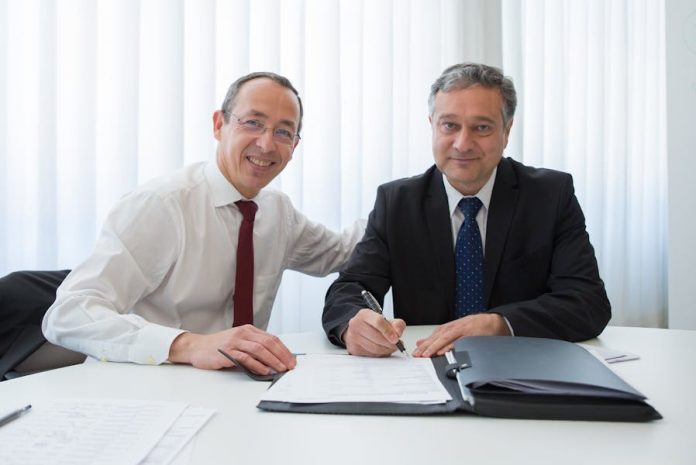 Photo by Kampus Production Two businessmen in suits signing a contract at a well-lit office table.