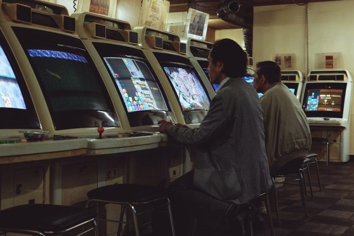 Photo by Ilya Yakubovich a man playing a video game in front of a row of slot machines
