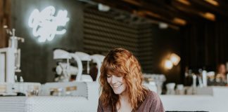 woman sitting on brown wooden chair while using silver laptop computer in room