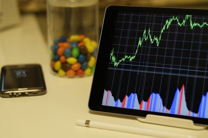 Photo by Burak The Weekender Tablet display of stock market data with smartphone and colorful candies on desk.