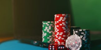 Close-up of casino chips and dice on a felt table, next to a laptop for online gambling.