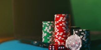 Close-up of casino chips and dice on a felt table, next to a laptop for online gambling.
