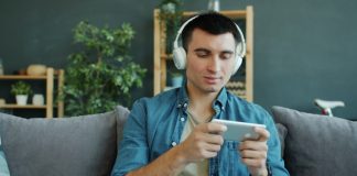 Kuinka digitaalinen eskapismi yhdistää aasialaisten draamojen fanit ja kasuaalit pelaajat Man wearing headphones plays game on smartphone.