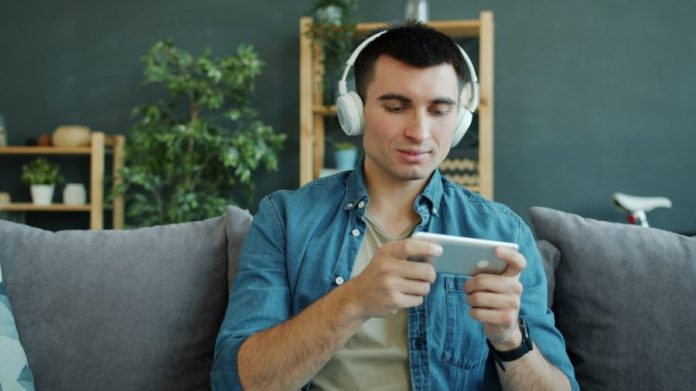 Photo by Vitaly Gariev Man wearing headphones plays game on smartphone.