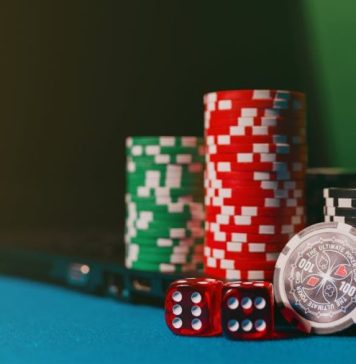 Close-up of casino chips and dice on a felt table, next to a laptop for online gambling.