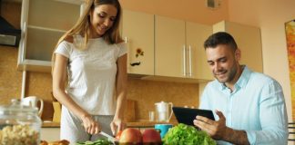 Couple preparing food and using tablet in kitchen.