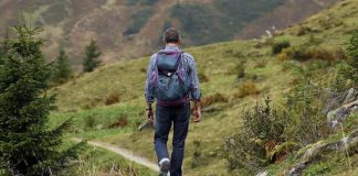 Discover the Benefits of a Walking Holiday in Europe A man with a backpack walks away down a gravel hiking trail through a green, grassy mountain landscape