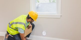 When to Schedule Furnace Service and Why Timing Matters? A construction worker in a hard hat inspects a floor vent indoors, ensuring quality and safety standards.