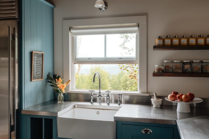 Photo by Clay Banks Farmhouse sink with stainless steel countertops and blue cabinets.