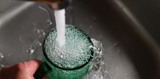 Tankless Water Heater Maintenance Made Simple for Efficiency a person's hand is holding a green cup with water coming out of it