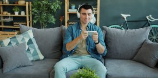 Man wearing headphones plays game on smartphone on phone.